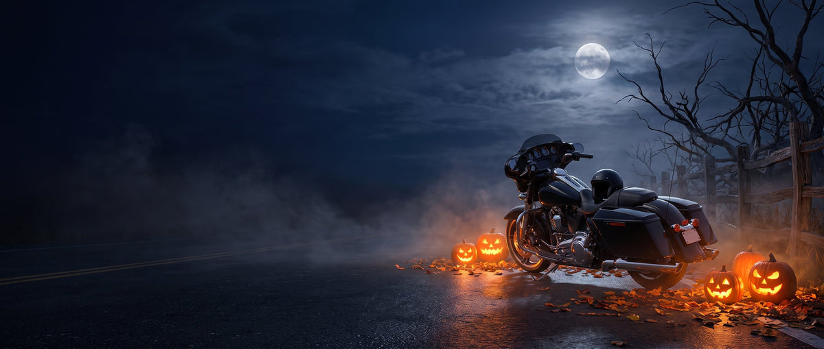 Black touring motorcycle parked on a foggy country road at night between glowing jack o lanterns